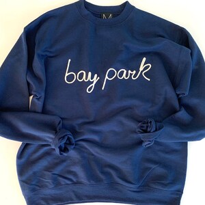 May include: A navy blue sweatshirt with the text "bay park" embroidered in white on the front.