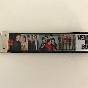 Puede incluir: Llavero en blanco y negro con una foto de la banda New Kids on the Block y el texto "New Kids on the Block" impreso sobre un fondo blanco.