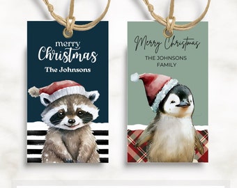 May include: Two printable Christmas gift tags featuring a raccoon and a penguin wearing Santa hats. The raccoon tag has a blue background with white stripes and the penguin tag has a green background with red plaid. The text on the tags reads "merry Christmas" and "The Johnsons Family".