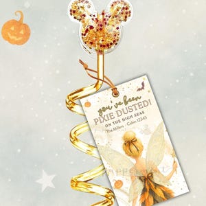 Può includere: Un decoro per cannuccia a spirale dorata con una testa di Topolino trasparente riempita di glitter arancioni e dorati, attaccato a un cartellino rettangolare con l'illustrazione di una fata e il testo you've been PIXIE DUSTED! ON THE HIGH SEAS The Millers Cabin 12345.