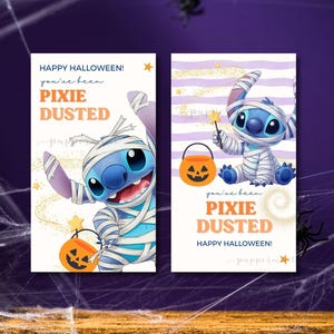 Può includere: Due cartoline rettangolari con un personaggio alieno blu avvolto in bende bianche come una mummia. Le cartoline mostrano il testo HAPPY HALLOWEEN e you've been PIXIE DUSTED in arancione e blu, insieme a un piccolo secchiello a zucca.