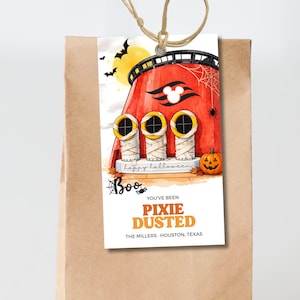 May include: A rectangular paper gift tag with a string, featuring a red cruise ship funnel with three mummy-wrapped smokestacks, a pumpkin, bats, and a spider web. Text reads: Happy Halloween, Boo, YOU'VE BEEN PIXIE DUSTED, THE MILLERS - HOUSTON, TEXAS.