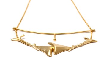 May include: A gold necklace with a geometric design. The necklace features a curved bar with a small ball at the end, and three abstract shapes hanging from the bar.