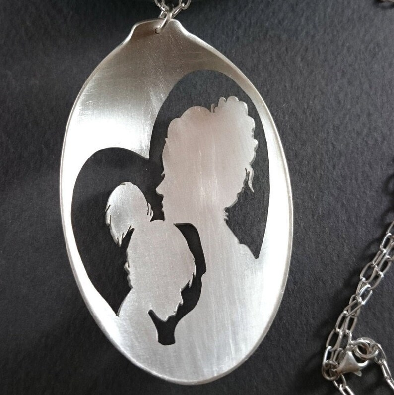 Pu&ograve; includere: Una collana con ciondolo in argento con un design a forma di cuore con un'incisione di una madre e un figlio.