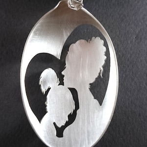 Pu&ograve; includere: Un cucchiaio d'argento con un ritaglio a forma di cuore che presenta una silhouette di una madre e un bambino. Il cucchiaio &egrave; un ciondolo e ha una catena d'argento.
