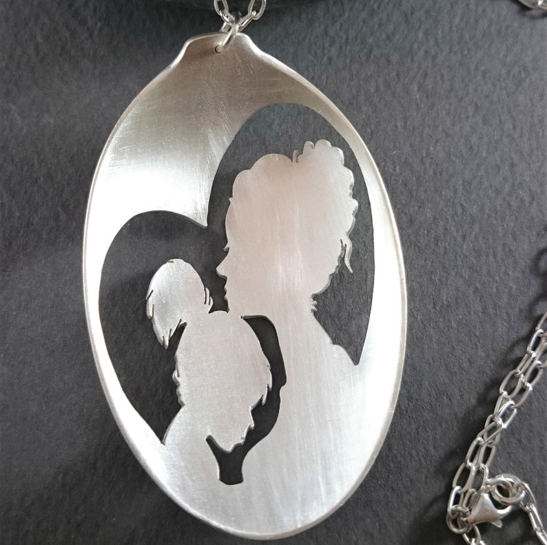 Pu&ograve; includere: Una collana con un ciondolo d'argento con un designo a forma di cuore con un'incisione di una madre e un bambino.