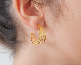 May include: Gold hoop earrings with a delicate, layered design. The earrings are made of thin metal and have a slightly curved shape.