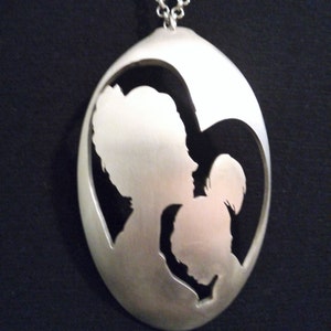 Pu&ograve; includere: Una collana con un ciondolo a forma di cucchiaio d'argento, con un designo a forma di cuore ritagliato che rappresenta una madre e un bambino.