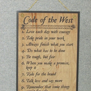 May include: A wooden sign with a black frame and the text "Code of the West" in a decorative font. The sign lists ten rules of conduct, including "Live each day with courage" and "Know where to draw the line".