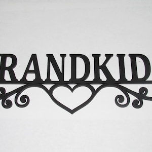 May include: Black wooden sign with the word "GRANDKIDS" in bold letters. The letters are connected by a decorative flourish with a heart shape in the center. The sign is designed for wall decor.