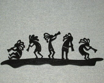 May include: Black silhouette wall art depicting five Native American figures playing flutes. The figures are in a line, facing right, and are standing on a black base.