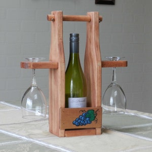 May include: Wooden wine bottle and glass holder with a painted grape design. The holder has two slots for glasses and a space for a bottle of wine. The bottle is labeled "Les Parelle" and is a white wine.