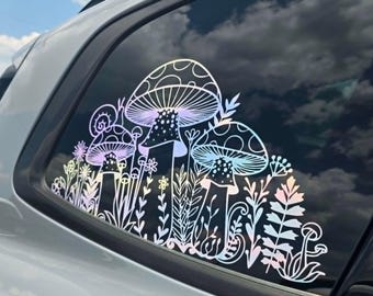 May include: An iridescent decal applied to a car window featuring a detailed line art illustration of various mushrooms, small flowers, and leafy plants. The design displays a reflective, multi-colored finish that shifts in light across the glass.