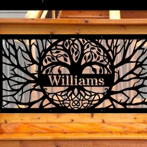 May include: Black metal tree of life wall art with the name "Williams" cut out in a banner across the center. The tree design features intricate branches, leaves, and a circular base. The artwork is mounted on a wooden structure.