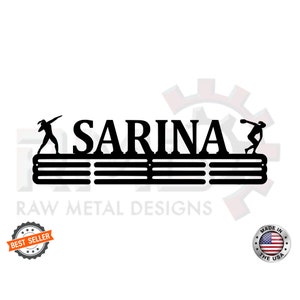 May include: Black metal medal display rack with the name "SARINA" and two silhouettes of athletes. The rack has five horizontal bars for hanging medals. The text "RAW METAL DESIGNS" is below the rack. The image also includes a "BEST SELLER" badge and a "MADE IN THE USA" badge.