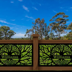 May include: A decorative wooden fence with two panels featuring a black tree of life design. The name "Williams" is displayed on each panel. The fence is set against a backdrop of green grass, trees, and a blue sky.