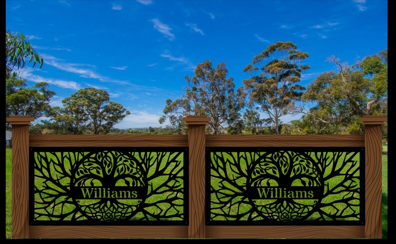 May include: A decorative wooden fence with two panels featuring a black tree of life design. The name "Williams" is displayed on each panel. The fence is set against a backdrop of green grass, trees, and a blue sky.