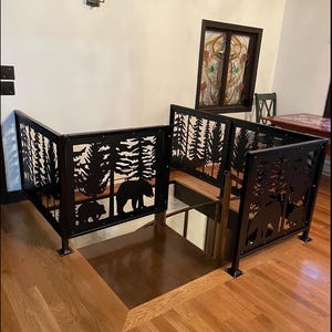 May include: Black metal stair railing with a forest and bear silhouette design. The railing features a series of panels with cut-out images of trees and bears. The railing is installed on a wooden staircase with hardwood flooring.