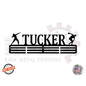 May include: Black metal medal display rack with the name "TUCKER" in large letters. The rack has five horizontal bars for hanging medals.  Two silhouettes of athletes are on either side of the name.  The words "BEST SELLER" and "MADE IN THE USA" are in circles at the bottom of the image.