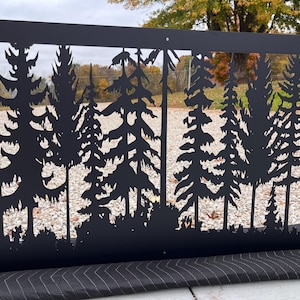 May include: Black metal wall art featuring a forest silhouette design. The rectangular piece has a cut-out of various trees and foliage. The artwork is held by a hand, showcasing the intricate details of the laser-cut design, perfect for outdoor or indoor decor.