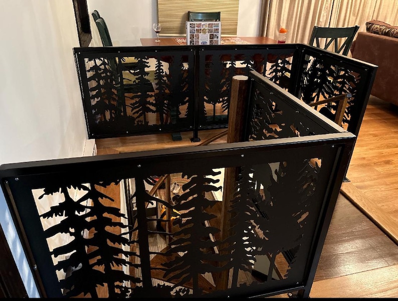 May include: Black metal room divider with a forest silhouette design. The divider is composed of multiple panels, each featuring cut-out images of trees. The panels are framed with a black border and are connected to create a cornered structure.