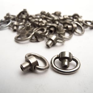 Può includere: Un mucchio di moschettoni girevoli in metallo argentato con un anello rotondo e un piccolo perno. I moschettoni sono disposti in modo casuale su una superficie bianca.