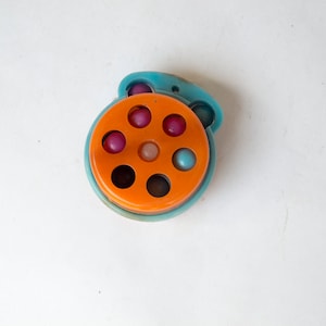 Può includere: Un giocattolo di plastica blu e arancione con una ruota girevole e sei palline colorate all'interno.