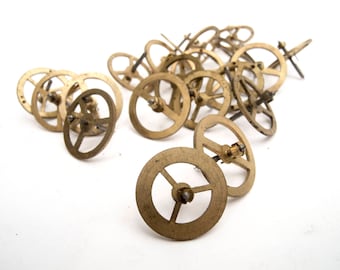 May include: A pile of small, gold-coloured metal gears with a central hole and three spokes. The gears are arranged in a random pattern on a white background.