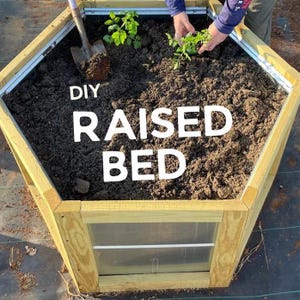 May include: A hexagonal raised garden bed constructed from light-colored wood and metal panels, filled with dark soil and small green plants. A metal shovel rests in the soil. The text DIY RAISED BED is printed in white over the center of the bed.
