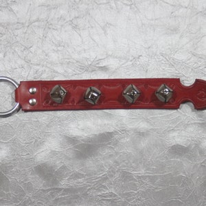 May include: Red leather strap with four silver bells attached. The strap has a silver ring on one end and a pointed end on the other.