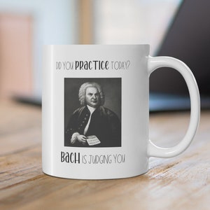 May include: White ceramic mug featuring a black and white image of Johann Sebastian Bach and the text "Did you practice today? Bach is judging you."