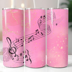 Op de afbeelding: Drie roze roestvrijstalen bekers met een muzieknootontwerp. De bekers hebben een roze en gouden glitterachtergrond met zwarte muzieknoten en een solsleutel.