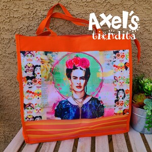 May include: Orange tote bag with a Frida Kahlo portrait, floral crown, and green halo. The bag has orange handles and a Day of the Dead skull pattern. The text "Axel's tiendita" is visible. The bag is suitable for carrying items.