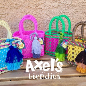 May include: A collection of colorful woven tote bags with matching handles and decorative tassels. The bags are in various bright colors, including blue, pink, green, and yellow. The text "Axel's tiendita" is displayed in white.