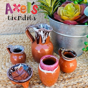 May include: A set of miniature terracotta pottery including a pitcher, two small handled jugs, and a small bowl with a leaf design. Each piece features a glossy brown finish with white or pink drip-style glaze accents along the rims.