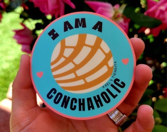 Puede incluir: Una pegatina redonda con fondo azul claro y borde rosa. La pegatina presenta el texto "I AM A CONCHAHOLIC" en negro, con un diseño de pan concha en el centro. También se incluyen dos corazones rosas.
