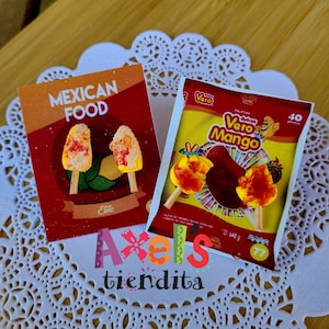 May include: Two packages of Mexican candy, one with "Mexican Food" and "Elote" text, and the other with "Vero Mango" text. The candy is on a white doily. The "Axels tiendita" logo is at the bottom.