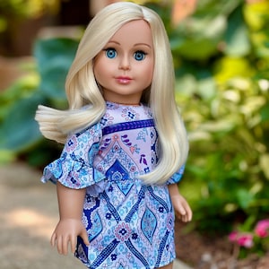 May include: A doll with long blonde hair wearing a blue and purple patterned dress with a ruffled neckline.