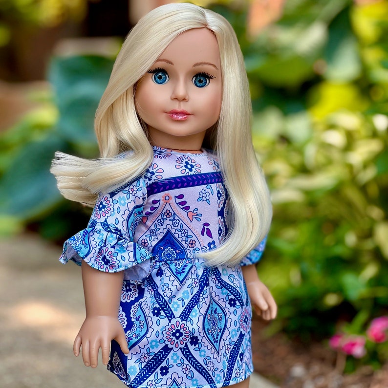 May include: A doll with long blonde hair wearing a blue and purple patterned dress with a ruffled neckline.