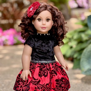 May include: A doll with brown curly hair and brown eyes, wearing a red flower hair accessory. The doll is dressed in a black velvet short-sleeved top with silver studs at the neckline and a red skirt featuring a black damask pattern.