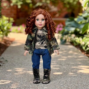May include: A doll with long curly auburn hair and green eyes, wearing a camouflage print jacket over a matching camouflage t-shirt, dark blue denim jeans, and camouflage print lace-up boots with black laces, standing in an upright position.