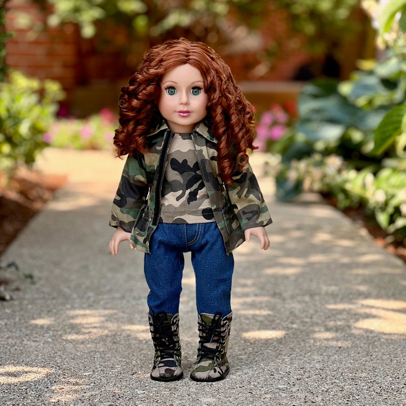 May include: A doll with long curly auburn hair and green eyes, wearing a camouflage print jacket over a matching camouflage t-shirt, dark blue denim jeans, and camouflage print lace-up boots with black laces, standing in an upright position.