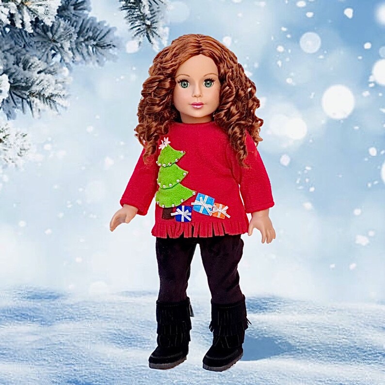 May include: A red Christmas sweater with a green Christmas tree and presents on it. The sweater is being worn by a doll with long, curly red hair. The doll is wearing black pants and black boots.