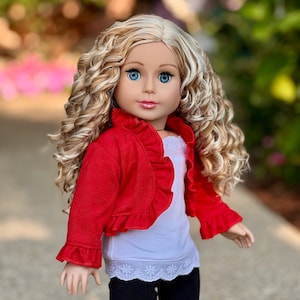 May include: A doll with long, curly blonde hair wearing a red ruffled cardigan, a white tank top with lace trim, and black pants.