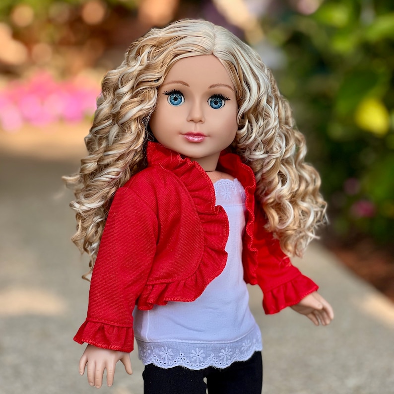 May include: A doll with long, curly blonde hair wearing a red ruffled cardigan, a white tank top with lace trim, and black pants.