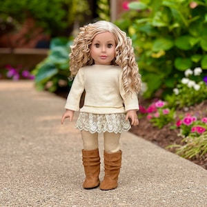 May include: A doll with long blonde curly hair wearing a white sweater, a lace skirt, and brown boots.