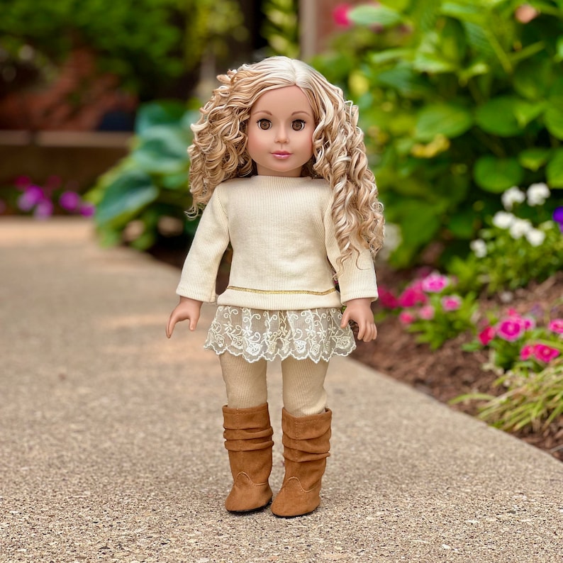 May include: A doll with long blonde curly hair wearing a white sweater, a lace skirt, and brown boots.
