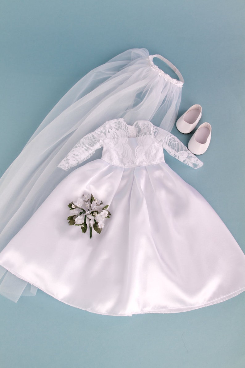May include: A white satin bridal gown with lace sleeves and a veil. The gown has a bouquet of white flowers and green leaves. The set also includes a pair of white shoes.