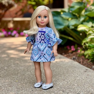 May include: A doll with long blonde hair wearing a blue and white patterned dress with ruffled sleeves and silver shoes.