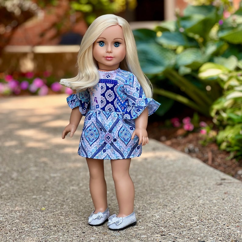 May include: A doll with long blonde hair wearing a blue and white patterned dress with ruffled sleeves and silver shoes.